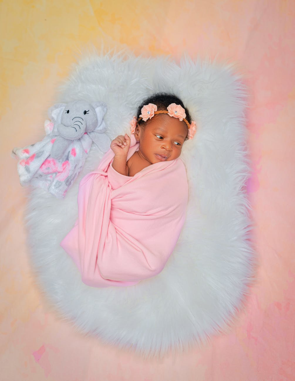 cute baby in pink swaddle lying on blue fur blanket